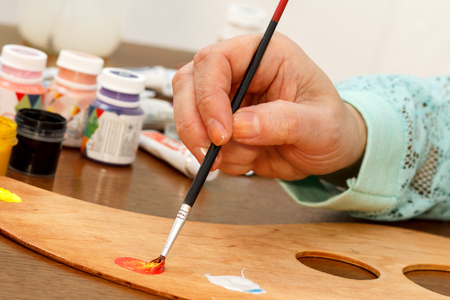 A womans hand mixing red and yellow paints on the paletteの写真素材