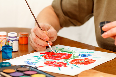 Woman's hand painting poppy flowers on a white sheet of paperの写真素材