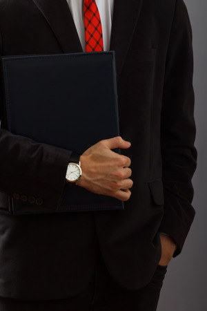 Young man in black suit holding the folder in his hand with wristwatchの写真素材