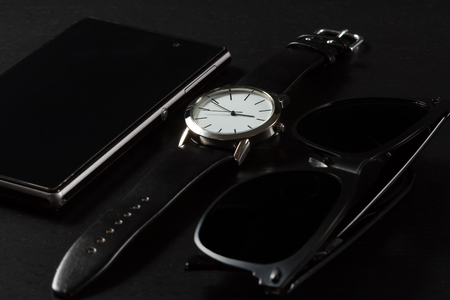 Watch with a leather strap, sell phone, black sunglasses on a black backgroundの写真素材