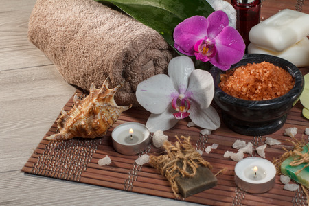 Spa and wellness setting with orchid flowers, bowl with sea salt, seashell, bottle with aromatic oil, soap, candles and towels on bamboo napkinの写真素材