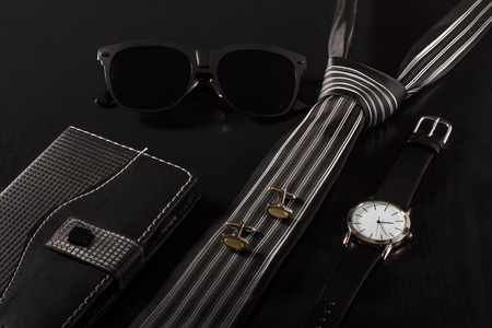 Notebook in leather cover, sunglasses, tie, cuff-links, watch with a leather strap on a black backgroundの写真素材