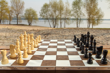 Chess board with chess pieces on river embankment background. Outdoors chess game with wooden chess piecesの写真素材