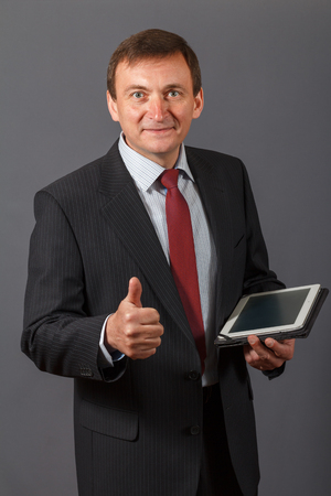 Confident and friendly elegant handsome mature businessman standing in front of a grey background holding a notebookの写真素材