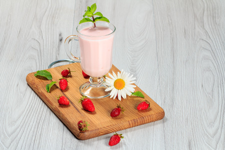 Glass of delicious milk shake with mint and fresh strawberries,  chamomile on a wood cutting boardの写真素材
