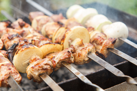 Meat and onions on skewers, zucchini and mushrooms on skewer are grilling on charcoal. Cooking a dish of shish kebab at barbecue. Picnic, street food. Selective focusの写真素材