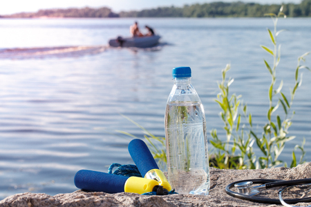 Jump rope, stethoscope and bottle with water on rock with river embankment background. Summer, active lifestyleの写真素材