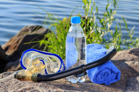 Bottle with water, towel,  mask for diving and snorkel tube on rock with sea shore background. Summer, active lifestyleの写真素材