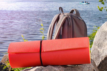 Hiking backpack and camping mat on rock with river embankment background. Adventure, summer, tourism active lifestyle. Equipment for outdoor activities. Travel gearの写真素材