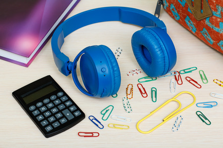 School supplies. School backpack, book, color paper clips, headphones and calculator on wooden table. Top view. Back to school concept.の写真素材