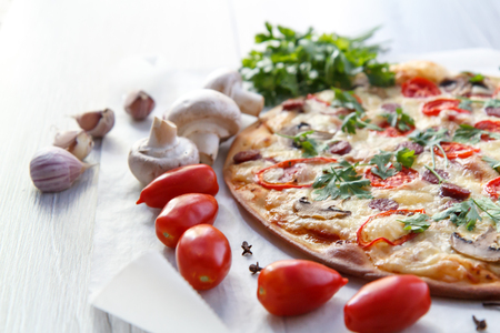 Fresh homemade pizza with tomatoes, salami, cheese and mushrooms with food ingredients and spices for cooking  on piece of baking paper. Closeupの写真素材