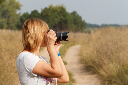 Young woman holding digital camera and taking pictures of the summer landscape at rural roadの写真素材