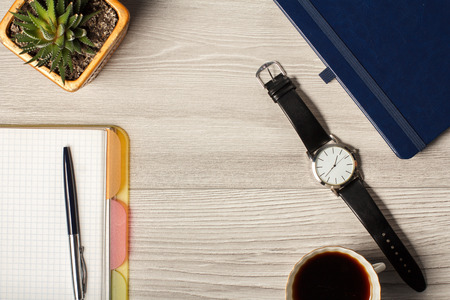 Notebook, men's watch, pen, cup of coffee and houseplant in a pot on a grey wooden background. Top viewの写真素材