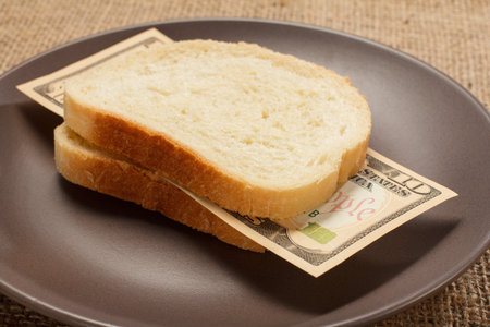 Two slices of bread with ten American dollars bill as hamburger of money on brown plate. Money ready to be eaten. Concept of financial relationshipsの写真素材