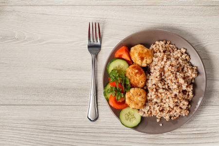Plate with buckwheat, fried meat cutlets, pieces of fresh cucumbers and tomatoes decorated with branch of fresh parsley with knife fork. Top viewの写真素材