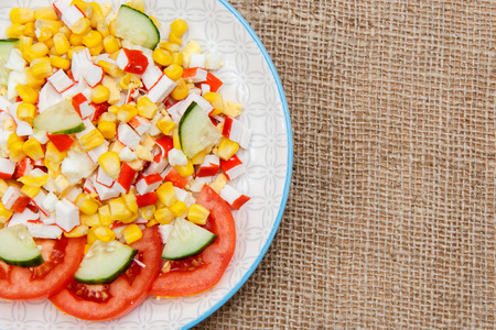Salad with sliced crab sticks, boiled corn and fresh tomato and cucumber on plate. Top view with copy spaceの写真素材