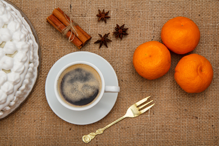 Biscuit cake decorated with whipped cream, cup of coffee, fork, oranges, star anise and cinnamon on table with sackcloth. Top viewの写真素材