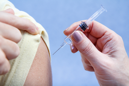 Hand of doctor holding syringe for vaccination to upper arm of patient for flu sickness prevention. Selective focus on syringeの写真素材