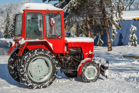 Red tractor removing snow from the footpaths in the city park after snowfall. Winter timeの写真素材
