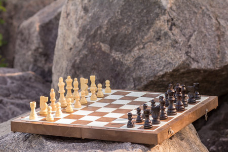 Chess board with chess pieces on stone with big rocks on the background. Outdoors chess game