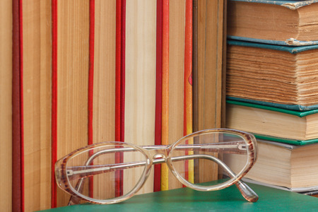 Glasses and many old hardback books on wooden shelf. Education background. Library conceptの写真素材