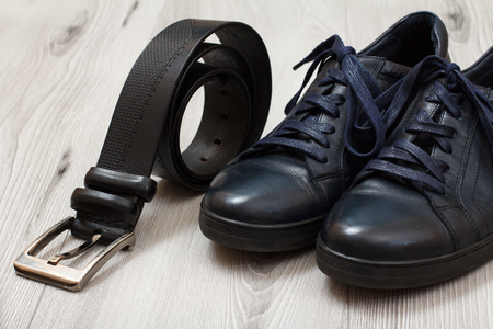 Pair of black leather men's shoes with laces and leather belt for men on grey wooden board. Men's accessoriesの写真素材