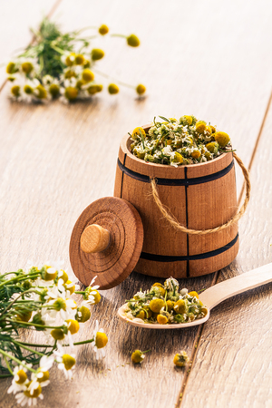 Little wooden barrel with dry flowers of chamomile and bouquet of fresh chamomiles on wooden boardsの写真素材