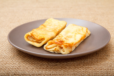 Homemade pancakes filled with cottage cheese on plate with sackcloth on backgroundの写真素材