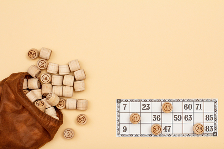 Wooden lotto barrels with brown bag and game card on beige background. Board game lotto. Top view with copy spaceの写真素材