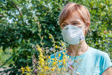 Woman in protective mask holding bouquet of wildflowers and trying to fight allergies to pollen. Woman protecting her nose from allergens. Allergy concept.の写真素材