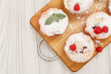 Homemade fruit muffins sprinkled with powdered sugar and fresh raspberries on wooden cutting board. Top view with copy spaceの写真素材