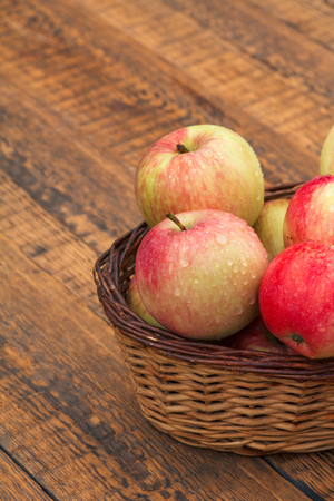 Red apples in wicker basket on wooden boardsの写真素材