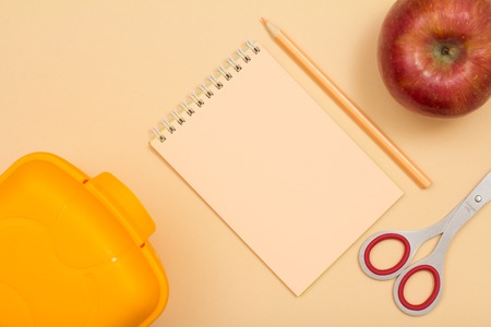 School supplies. Lunch box, notebook, color pencil, apple and scissors on beige background. Top view. Back to school concept. Pastel colorsの写真素材