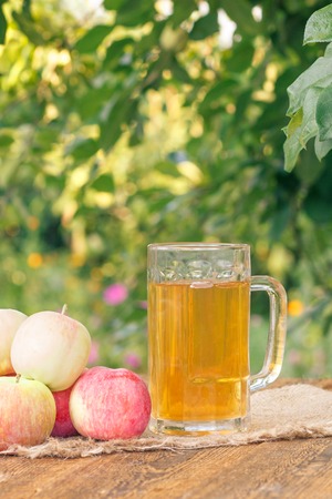 Just picked apples and apple cider in glass goblet on wooden boards with leaves of apple tree on the background. Just harvested fruits. Organic drinksの写真素材