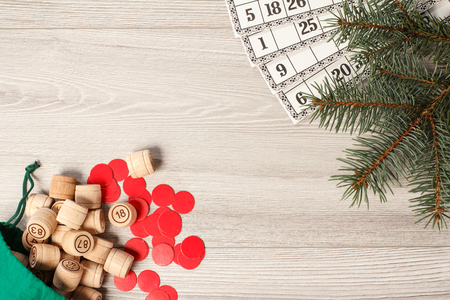 Board game lotto. Wooden lotto barrels with green bag, game cards and red chips for a game in lotto, Christmas fir tree branches and cones. Top viewの写真素材