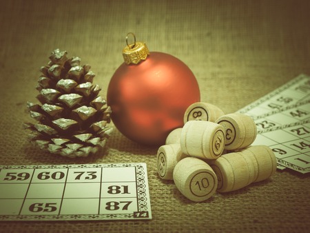 Board game lotto. Wooden lotto barrels and game cards for a game in lotto, Christmas toy ball and fir cone on sackcloth. Color toning effect.の写真素材