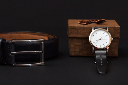 Leather belt with metal buckle, watch with a black leather strap and brown gift box on blackの写真素材