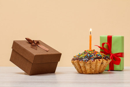Tasty birthday muffin with chocolate glaze and caramel, decorated with burning festive candle and...