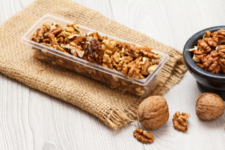 Peeled walnuts in plastic container and stone bowl with sackcloth on a wooden background. Useful nutritious protein product. Top view.の写真素材
