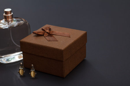 Cologne for men, brown gift box and cufflinks on black background. Accessories for men.