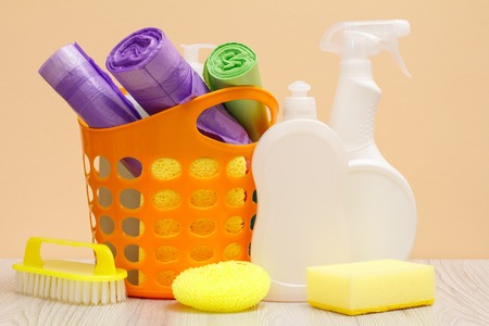 Plastic bottles of dishwashing liquid, glass and tile cleaner, detergent for microwave ovens and stoves, basket with garbage bags, sponge and brush on beige background. Washing and cleaning concept.の写真素材