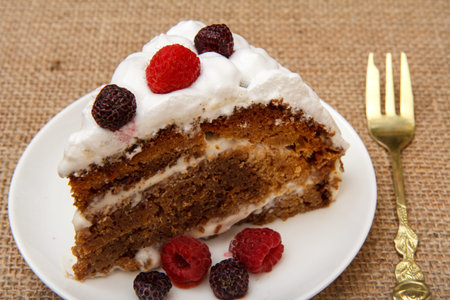 Plate with slice of homemade biscuit cake decorated with whipped cream and raspberries on plate,...