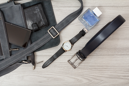 Leather shoulder bag for men with mobile phone and wallet on it, wristwatch, men's cologne and belt for men with gray woodenの写真素材