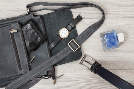 Leather shoulder bag for men with wallet and wristwatch on it, men's cologne and belt for men with gray woodenの写真素材