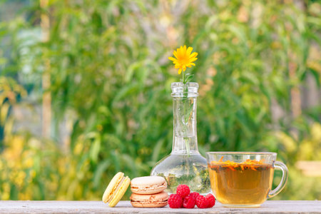Cup of green tea, delicious macaroons cakes of different color, fresh raspberries and calendula...