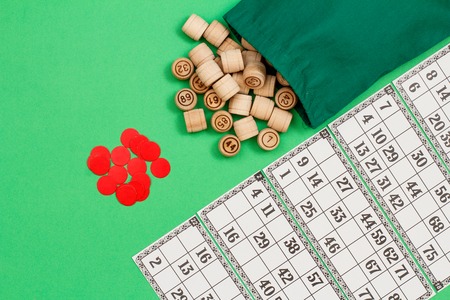 Wooden lotto barrels with cloth bag, game cards and red chips on green background. Board game lotto. Top view.の写真素材