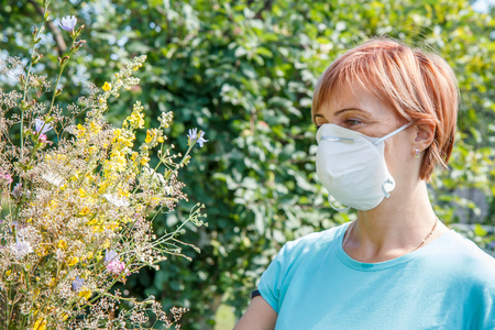 Woman in protective mask holding bouquet of wildflowers and trying to fight allergies to pollen.の写真素材