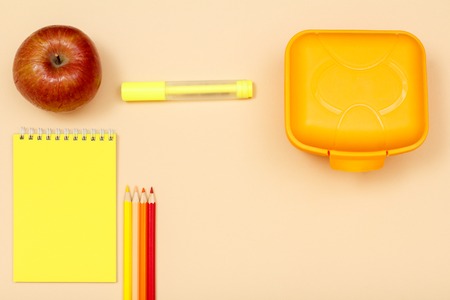 Apple, notebook, color pencils, felt pen and lunch box on beige background. Top view. Back to school concept. School supplies.の写真素材