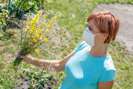 Woman in protective mask holding bouquet of wildflowers and trying to fight allergies to pollen.の写真素材