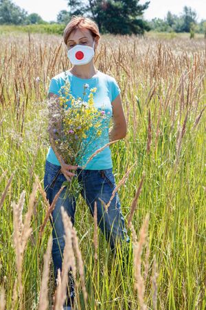 Woman in protective mask holding bouquet of wildflowers and trying to fight allergies to pollen.の写真素材